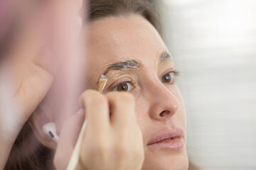 Fototapeta premium Coloring and lamination in a beauty salon for a beautiful client who came for eyebrows. eyebrow care. Master of applying paint with a brush