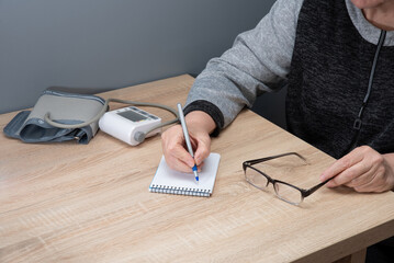 woman independently measures her blood pressure at home and records the readings in a notebook