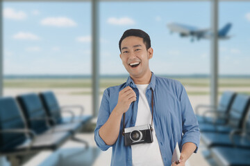 Happy Asian man holding passports and boarding passes at the airport terminal, excited and ready...