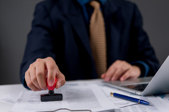 Businessman stamping official documents for approval. Legal authorization and certified paperwork concept in office or financial institution environment.
