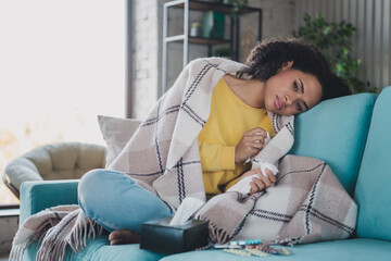 Young sad woman resting at home on a cozy couch wrapped in a blanket, feeling unwell