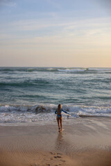A woman is leisurely walking along the beach while holding a surfboard
