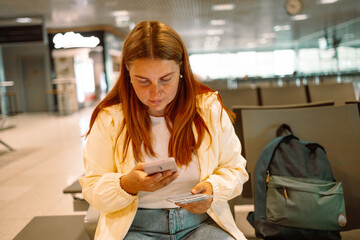 Close up of businesswoman checking flight ticket on phone while holding passport and boarding pass....