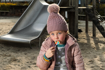 The girl in the winter hat eats lollypop.