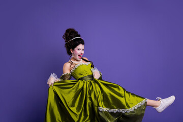 Woman wearing a green historical dress in playful pose against a vibrant purple backdrop