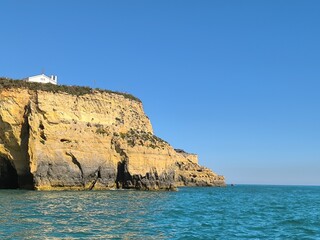 The rugged cliffside rises above the turquoise sea, creating a dramatic coastal scene with clear waters below.