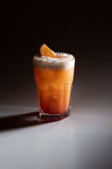 Fresh tequila sunrise cocktail with orange slice and ice sparkling bubbles, on dark shadowy background, stock