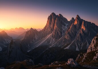 A breathtaking view of a majestic mountain range under a vibrant sunset sky. The mountains are illuminated by the golden light, casting shadows and adding depth to the scene.