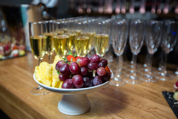 A bowl of fruits placed against the backdrop of wine glasses