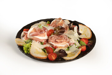 caesar salad with lettuce, raw ham, bread, oil, tomatoes and parmesan cheese served in a black plate on white background