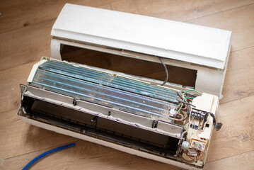 Dirty and disassembled wall-mounted air conditioner unit, showing internal components and dust,...