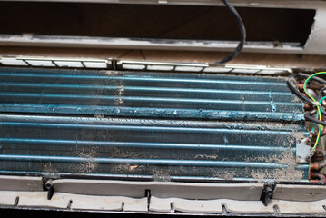 Dirty and disassembled wall-mounted air conditioner unit, showing internal components and dust, placed on wooden floor for repair or cleaning.