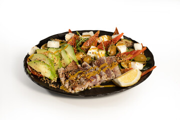 caesar salad with avocado olives, lemon, feta cheese, oil, arugola and parmesan cheese served in a black plate on white background