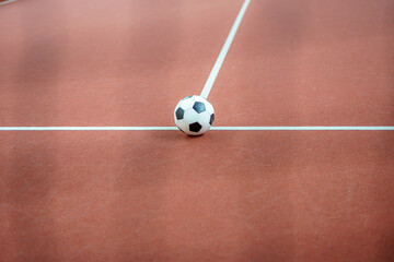 A soccer ball in the middle of the lines on a maroon field.