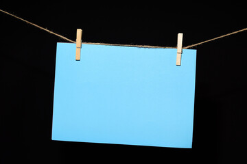 Cartulina celeste colgada con pinzas sobre fondo negro