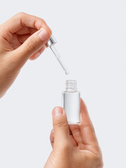 Close-up of hands dispensing serum into a clear glass bottle with a dropper on a clean background