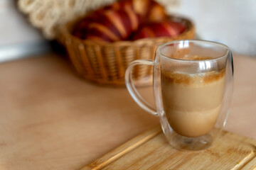 Cup of cappuccino on blurred background of croissants in wicker basket. Morning coffee with croissants.