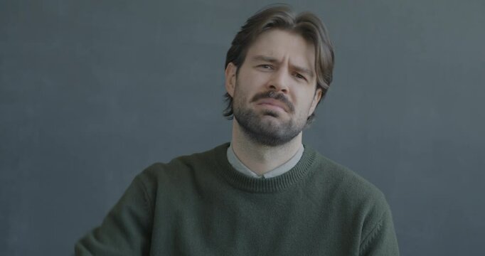 Portrait of displeased young man showing thumbs-down hand gesture looking at camera expressing disappointment on black color background.