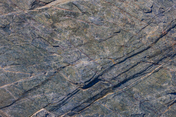 Foliated metamorphic rock with prominent fractures, natural texture, outdoor, daylight