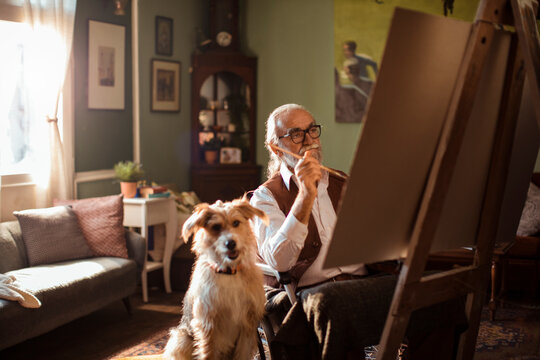 Senior artist in wheelchair painting at home with dog by his side