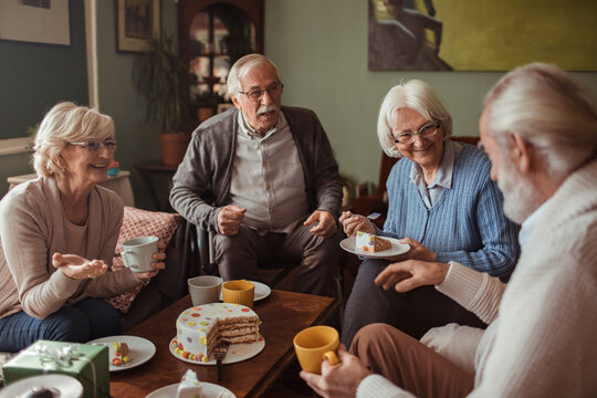 Happy group of senior friends enjoying coffee and cake together at home