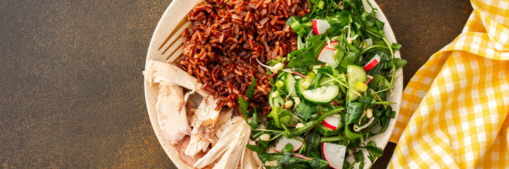 Delicious healthy breakfasts, chicken breast with red rice and salad mix with fresh seasonal organic vegetables and microgreens, top view of a plate with food and a cutting board with vegetables, bann