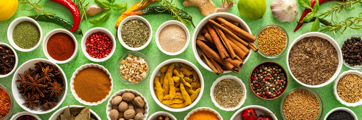 Fresh, multicolored spices and herbs set against a gentle green background, creating a vivid,...