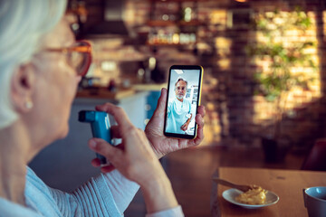 Senior woman using a mdi inhaler while talking to her doctor over a video call on her smart phone