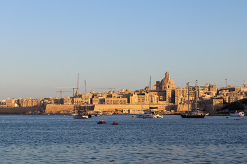 Valletta, Malta 28 September 2024: Valletta cityscape reflecting on the calm water during sunset with sailboats sailing on the Mediterranean sea