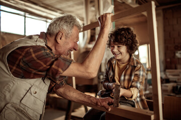 Grandfather teaching grandson woodworking in home workshop