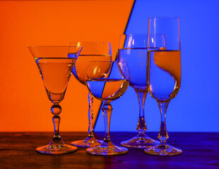Different glasses for alcoholic drinks on colorful background. Light refraction studio shot.   