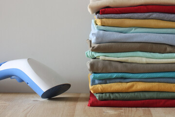 Steamer and stack of folded clothes resting on wooden table