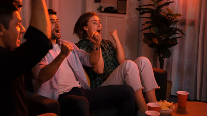 Family and colleague sitting at dark living room with red filter while cheering football team together. Caucasian people enjoy watching tv and giving high five to celebrate winning team. Convocation.