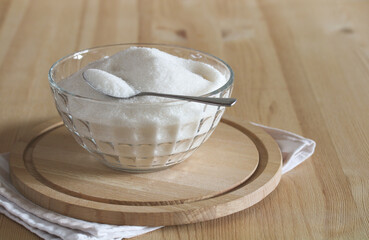 Glass bowl overflowing with white sugar on wooden board