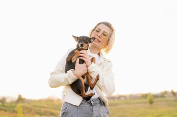 Woman holds in arms, hugs dog, smooth-haired Russian toy terrier, who ran away during walk in park. Concept lost pet, caring for dog