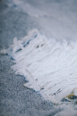 Close-up of ripped light blue denim fabric with frayed threads and visible tear
