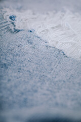 Close-up of ripped light blue denim fabric with frayed threads and visible tear