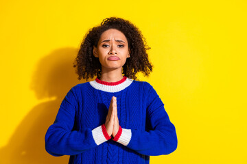 Young woman dressed in a blue sweater showing a thoughtful expression against a yellow background...