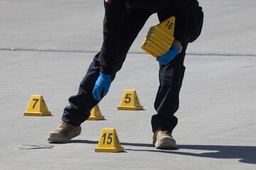 Law enforcement officer walking through a crime scene surrounded by evidence markers.