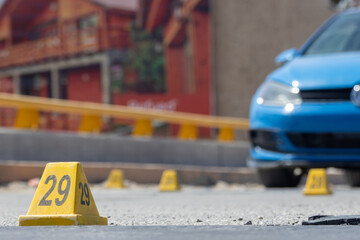 Multiple crime scene markers on a city street near a parked blue car