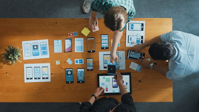 Top view of smart Ui designer brainstorming and planning about Ux Uo design or mobile interface wireframe design with diverse develop team. Caucasian programer walking and joining meeting.Convocation.