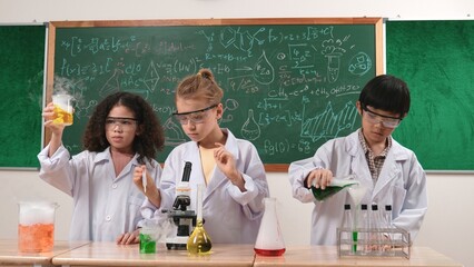 Children doing experiment in science lesson while standing at blackboard at laboratory. Happy student discovering and learning about biochemical liquid while inspecting and mixing sample. Pedagogy.