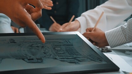 A focused team of engineers engages in a collaborative session, analyzing technical designs on a...