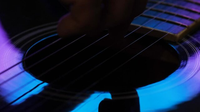 Fingers of a guitarist playing on strings in close-up, with the atmosphere and lighting of a performance, playing on a six-string guitar