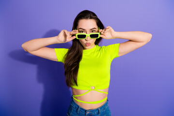 Young woman in vibrant outfit and sunglass posing playfully against a solid purple background