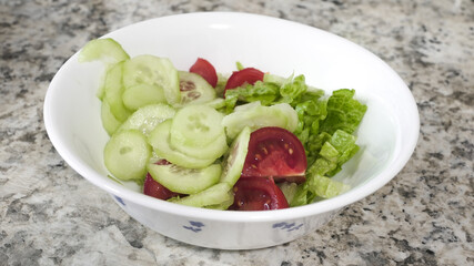 Fresh vegetable salad with cucumbers, tomatoes, and lettuce served in a bowl on a granite countertop