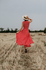 Girl in a hat and red dress in a wheat field with hay rolls