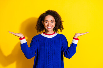 Cheerful young woman spreading her arms in a gesture on vibrant yellow background wearing stylish...