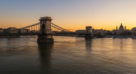 Fototapeta premium Chain Bridge Sunset Panorama - Stunning sunset view of the Chain Bridge in Budapest, Hungary, with the cityscape and river reflecting the golden light
