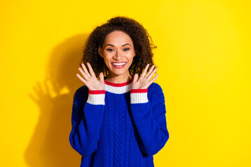 Cheerful young woman in blue sweater posing against vibrant yellow background with a playful...